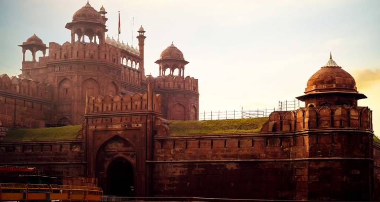 The imposing red sandstone walls and domes of the Red Fort glow in warm light against a clear sky.