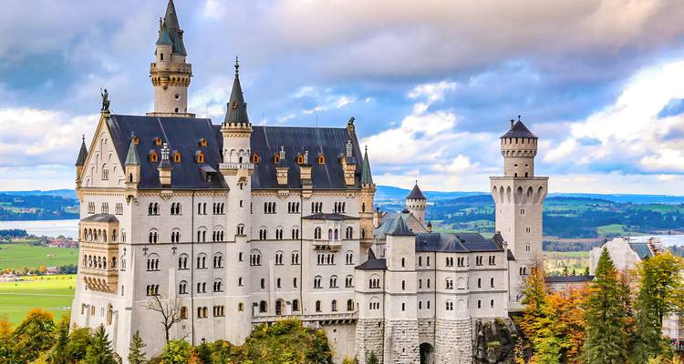 Iconic fairy-tale Neuschwanstein Castle rises above autumn trees with rolling countryside behind.