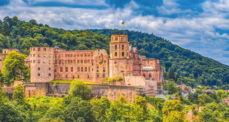 Heidelberg Castle dominates a forested hillside beneath a moody sky, overlooking the town below.