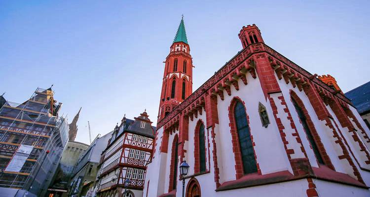 Historic red-and-white half-timbered buildings and a tall church spire in Frankfurt’s old town at dusk light.