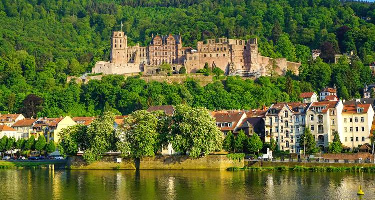 Evening light on Heidelberg Castle perched above riverside houses reflected in calm water.