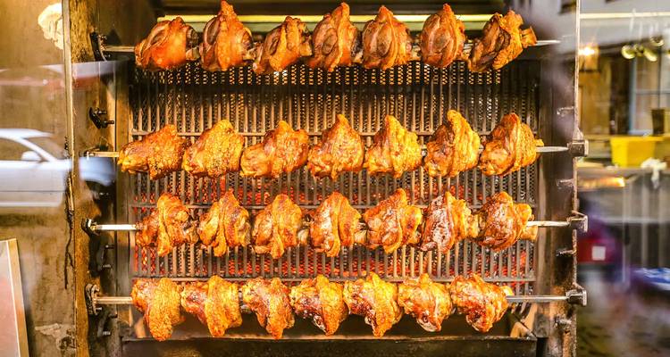 Rotisserie with rows of golden roasted chicken halves cooking behind glass.
