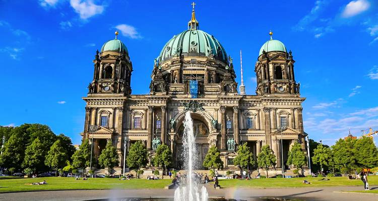 Berlin Cathedral with a lively lawn and fountain under a bright blue sky.