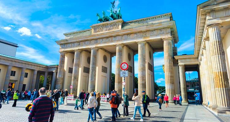 Visitors walk beneath the iconic Brandenburg Gate in Berlin on a bright day.