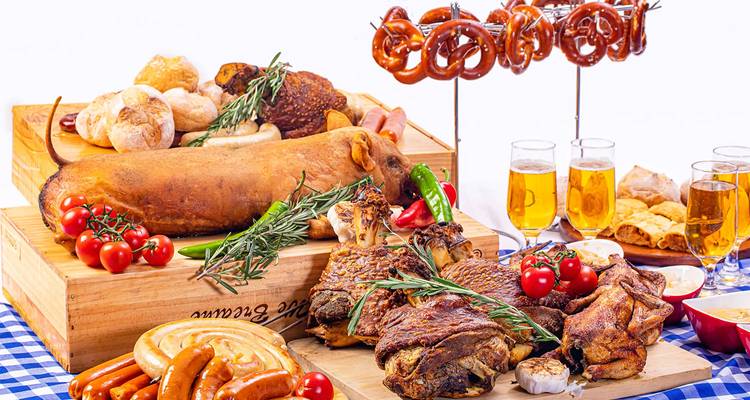 Traditional German feast with roast meats, pretzels and beer on a checkered tablecloth.