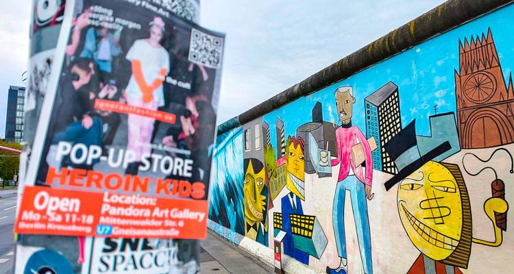 Colourful graffiti on the Berlin Wall’s East Side Gallery beside a street pole with posters.