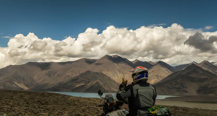 Personne sur une moto prenant une photo des montagnes lointaines près d'un lac.