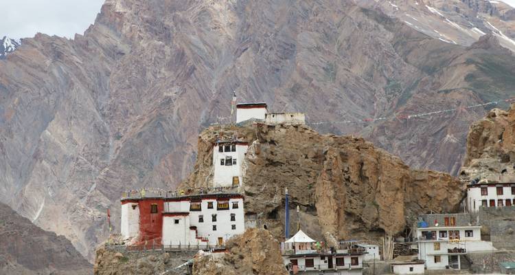 Plan rapproché d'un monastère sur une colline rocheuse avec des montagnes en arrière-plan.