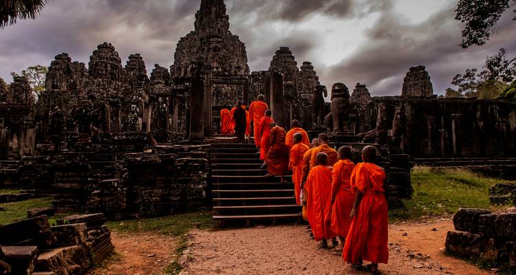 Monks in orange robes walking up steps to an ancient temple.