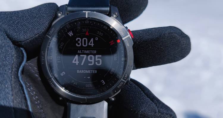 Close-up of altimeter watch reading 4 795 m held in gloved hand against snow.