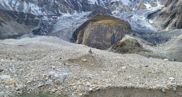 Solo trekker walking across a vast rocky glacier moraine with towering ice-covered peaks behind