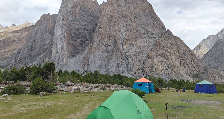 Remote campsite with colorful tents set on grassy plain below towering granite cliffs