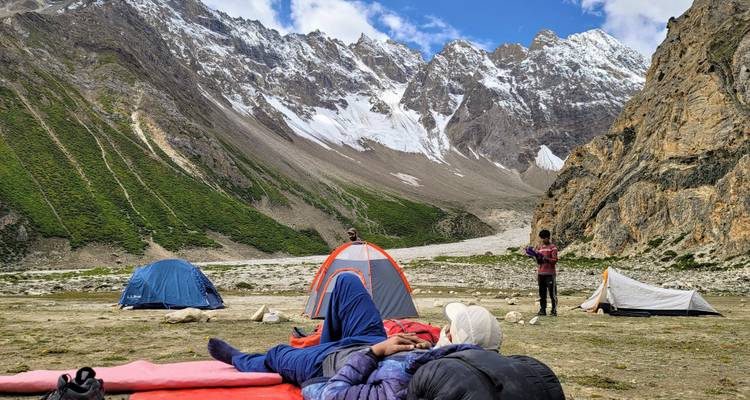 Trekkers resting on mats at a high-altitude base camp with snow-capped peaks in the background