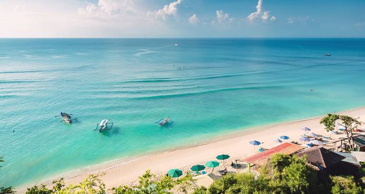 Idyllischer Tropenstrand mit türkisem Wasser, weißem Sand und farbenfrohen Sonnenschirmen auf Bali.