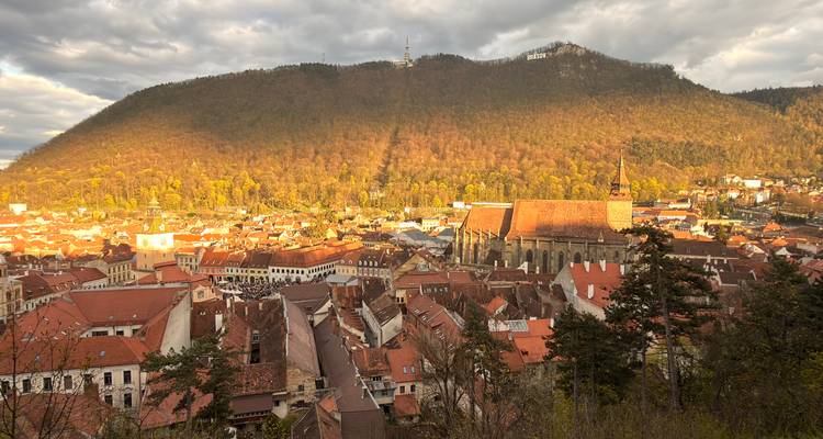 La lumière dorée illumine la vieille ville aux toits rouges de Brasov, située au pied d'une chaîne de montagnes boisée.