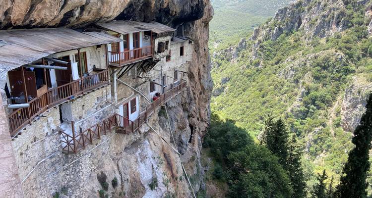 Un monastère à flanc de falaise construit dans la paroi rocheuse avec un décor montagneux en arrière-plan.