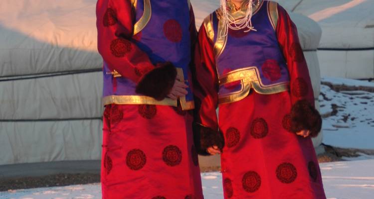 Zwei Personen in traditioneller mongolischer Kleidung stehen im Schnee.