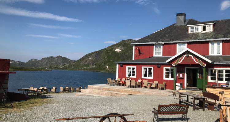 Maison rouge au bord d'un lac avec des montagnes en arrière-plan