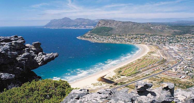 Vue côtière avec plage de sable et montagnes au loin.