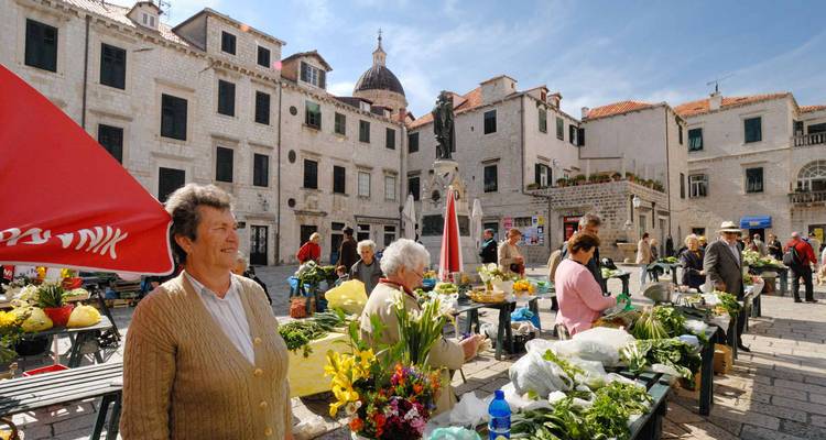 Bullicioso mercado de productos al aire libre en una plaza histórica de piedra con lugareños vendiendo flores y verduras