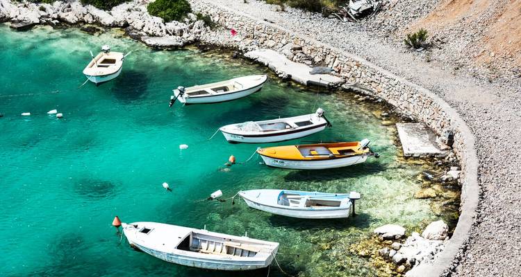 Fila de pequeños botes blancos flotando en una bahía turquesa cristalina junto a una orilla rocosa