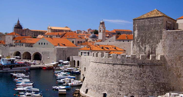 Muros de piedra y techos naranjas del casco antiguo de Dubrovnik elevándose sobre su puerto concurrido y embarcaciones