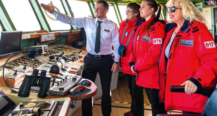 Los huéspedes recorren la cabina del barco, guiados por un oficial rodeado de instrumentos de navegación y ventanales panorámicos.