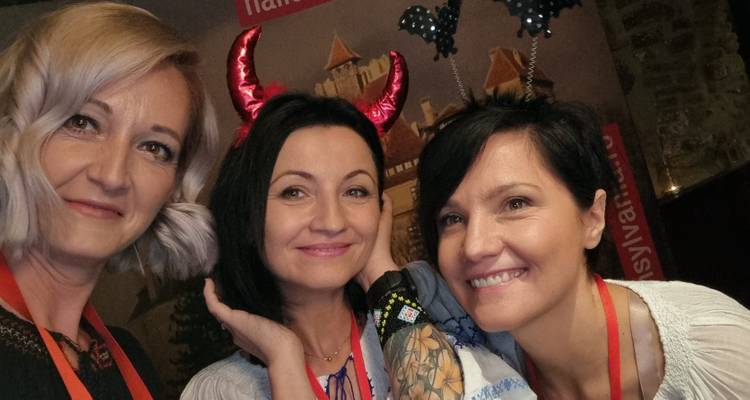 Selfie of three women wearing playful devil horns and bat headbands at an indoor Halloween party.