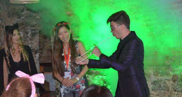 Magician in a stone cellar performing a rope trick amid green stage smoke while guests watch.