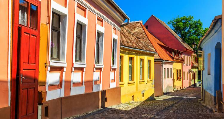 Brightly painted medieval houses line a narrow cobblestone street under clear blue skies.