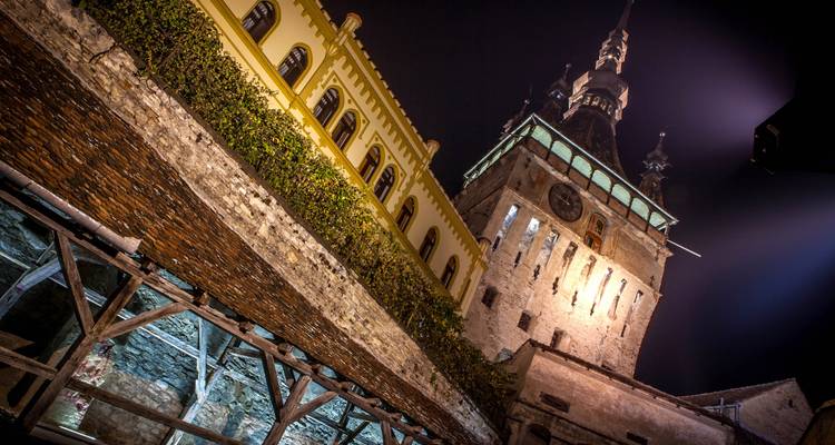 Upward night view of Sighisoara’s Clock Tower and surrounding walls dramatically lit against the dark sky.