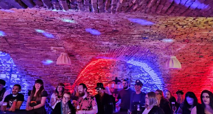 Crowd enjoys drinks and music under brick arches illuminated with red and blue club lighting.