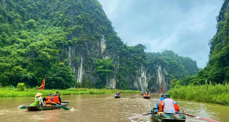 Menschen rudern in Booten entlang eines malerischen Flusses mit steilen Klippen.