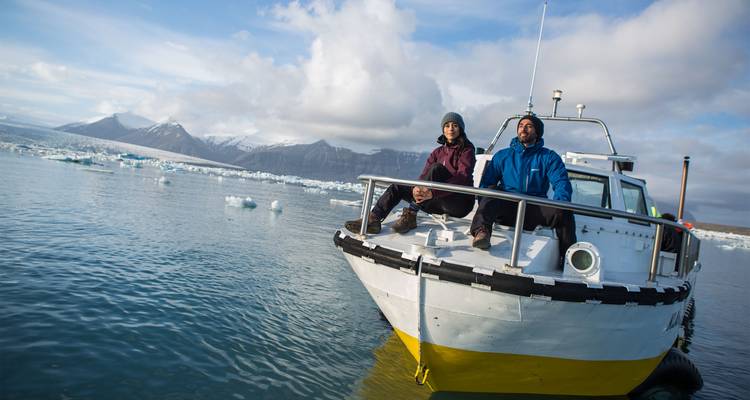 Pequeño bote con una pareja entre icebergs flotantes en la serena laguna glacial de Jokulsarlon.