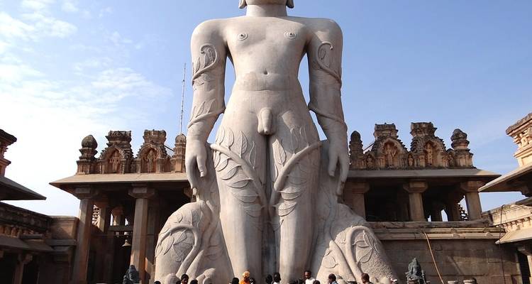 Eine große Steinstatue einer stehenden Figur mit Menschen an ihrer Basis, vor dem Hintergrund architektonischer Elemente.