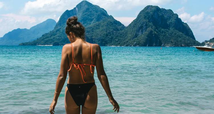 Person, die an einem Strand steht mit Bergen im Hintergrund.