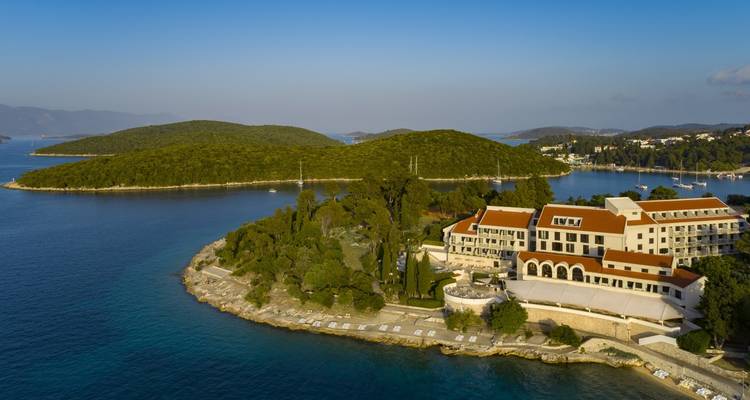 Aerial view of a forested peninsula with seaside resort buildings surrounded by turquoise Adriatic waters