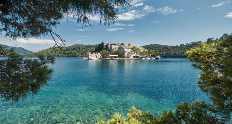 Medieval monastery on small islet in crystal-clear blue lake framed by pine branches