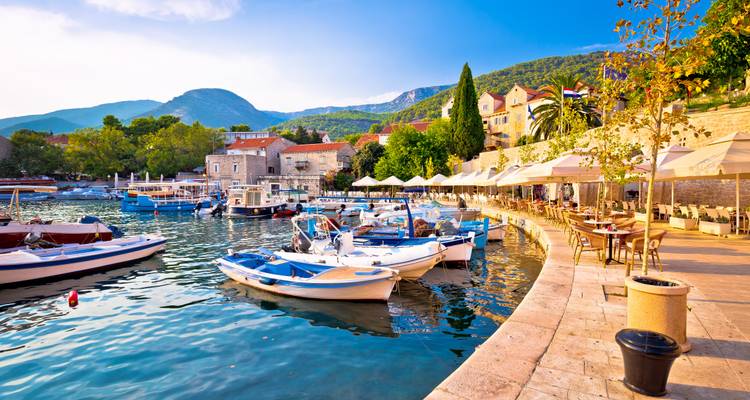 Charming Adriatic marina with small fishing boats, cafés and mountains beyond.