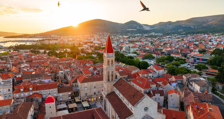 Sunset aerial of Trogir’s bell tower and terracotta rooftops glowing orange.
