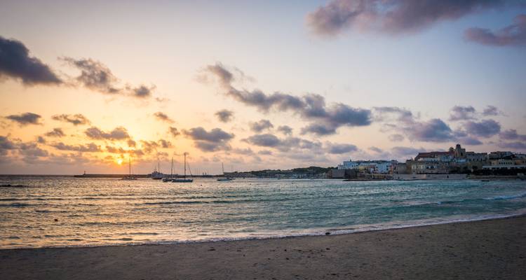 Zacht pastelachtig licht van zonsondergang over een kustplaats in Italië en aangemeerde zeilboten in een rustige baai.