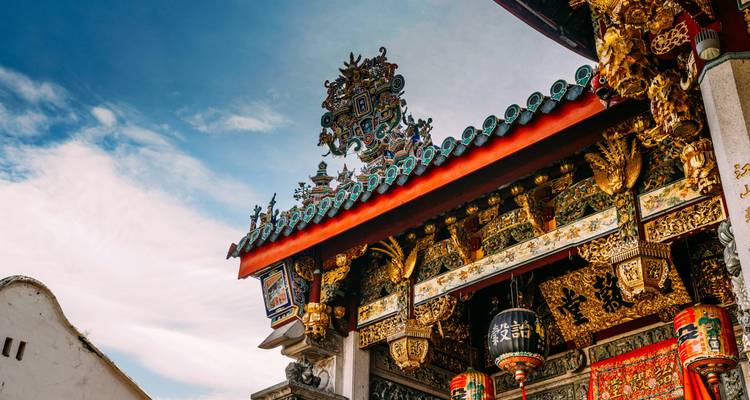 Ingewikkeld gesneden en geschilderd Chinees clanhuisdak met levendige kleuren tegen een blauwe hemel.