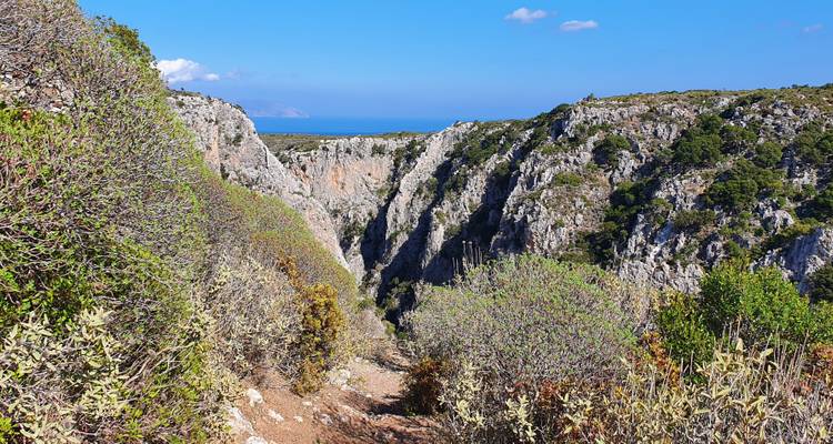 Paysage de canyon avec des falaises escarpées et une vue sur la mer sous un ciel bleu dégagé.