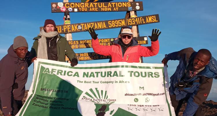 Groep op de top van de Mount Kilimanjaro met een toerbanner.