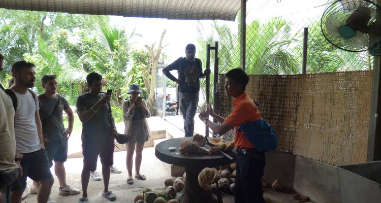 Menschen schauen zu, wie eine Person in einer Außenumgebung Kokosnuss zubereitet.