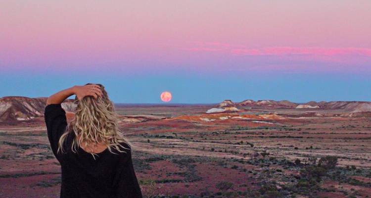 Persona observando la salida de la luna sobre un paisaje desértico.
