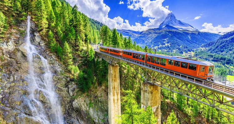 Trein die over een brug rijdt met een waterval en de Matterhorn.