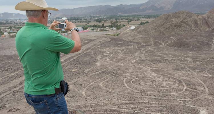 Man in a cowboy hat photographs one of the Nazca Lines geoglyphs from a desert viewpoint.