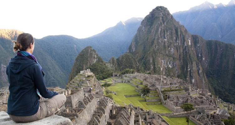 Woman meditates while overlooking the iconic ruins of Machu Picchu and surrounding green peaks.