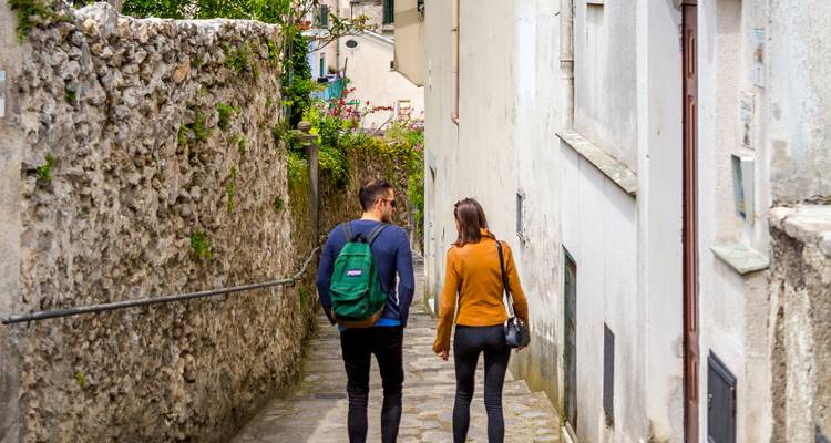 Un jeune couple se promène dans une ruelle pavée étroite bordée de murs rustiques et de maisons.